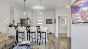 Una sala de estar moderna con un sofá, una mesa de centro y un comedor con sillas, y una cocina al fondo.