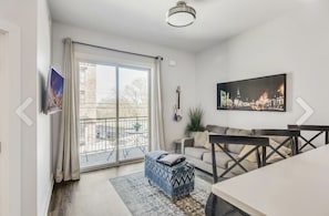 Relax in this stylish living room with a sofa set, dining table, and flat-screen TV, plus a sliding door leading to a balcony.