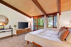 Une chambre à coucher avec un lit, une télévision, un bureau avec un ordinateur et une fenêtre donnant sur des arbres.