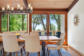 A dining area with a wooden table, chairs, and a view of trees through large windows.