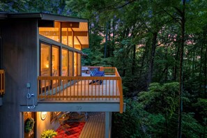 A modern house with a balcony overlooking a forest, a dining area with outdoor seating, and a visible number '39'.