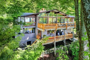 A multi-level wooden cabin with glass walls, surrounded by dense forest.