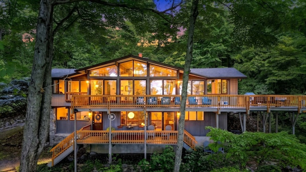 A two-story wooden cabin with a balcony, surrounded by dense forest.