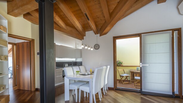 A modern kitchen with white cabinets, a dining area with white chairs, and a wooden ceiling. - New Deal - APT with Terrace & Jacuzzi (Palmanova)