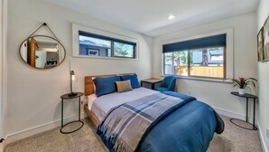 Een slaapkamer met een bed, een nachtkastje, een stoel, een ronde spiegel en twee ramen.