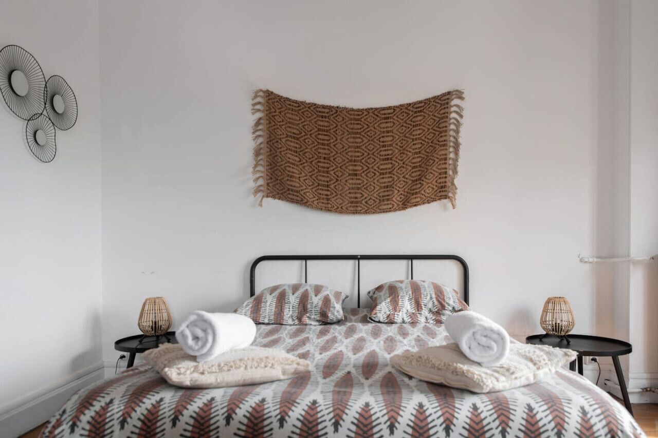 A neatly arranged bedroom with a patterned bedspread, two bedside tables with lamps, and a wall hanging above the bed.