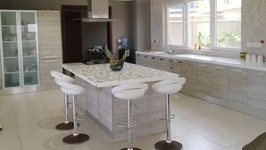 A modern kitchen with a central island, bar stools, a stainless steel range hood, and a window with a view of greenery. - A peaceful family home with brilliant sea views, set within private grounds. (Oshiyie)