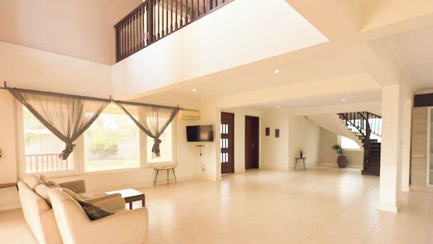 A spacious living area with a high ceiling, a staircase, and a balcony with a view. - A peaceful family home with brilliant sea views, set within private grounds. (Oshiyie)