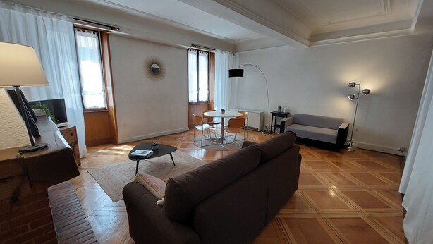 A modern living room with a sofa, a coffee table, a TV, and a dining area with chairs and a table.