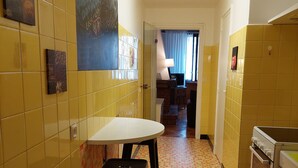 A narrow kitchen with yellow tiles, a white countertop, and a black stool.
