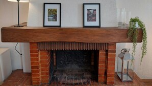 A fireplace with two framed pictures above it, a lamp to the left, and a potted plant to the right.