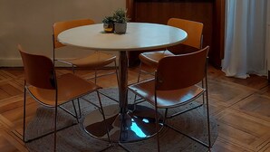 A dining area with a round table, four chairs, a floor lamp, and a window with curtains.