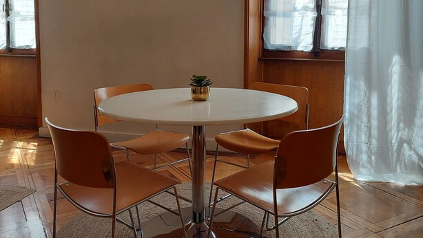 Una mesa redonda con seis sillas, una planta pequeña en maceta, un espejo montado en la pared y una lámpara colgante.