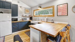 Eine kleine Küche mit dunkelblauen Schränken, einem weißen Kühlschrank, einer Mikrowelle und einem Holztisch.