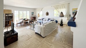 A spacious living room with a sofa, a coffee table, a TV, and a dining area with chairs and a table.