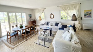 A spacious living room with a dining area, large windows, and a cozy sofa set.