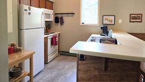 Cocina compacta con refrigerador, microondas, estufa y lavamanos. Hay una ventana con vista al exterior y armarios de madera.