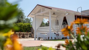 A covered outdoor seating area with white chairs and a table, surrounded by greenery. - Villa Ellea by pugliadamare (San Michele Salentino)