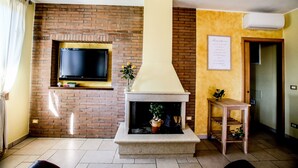 A living room with a brick fireplace, a mounted television, and a small table with a plant. - Villa Ellea by pugliadamare (San Michele Salentino)
