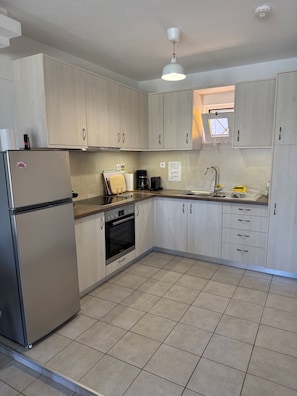 A kitchen with light wood cabinets, a stainless steel refrigerator, a built-in oven, a sink, and a window above the sink.