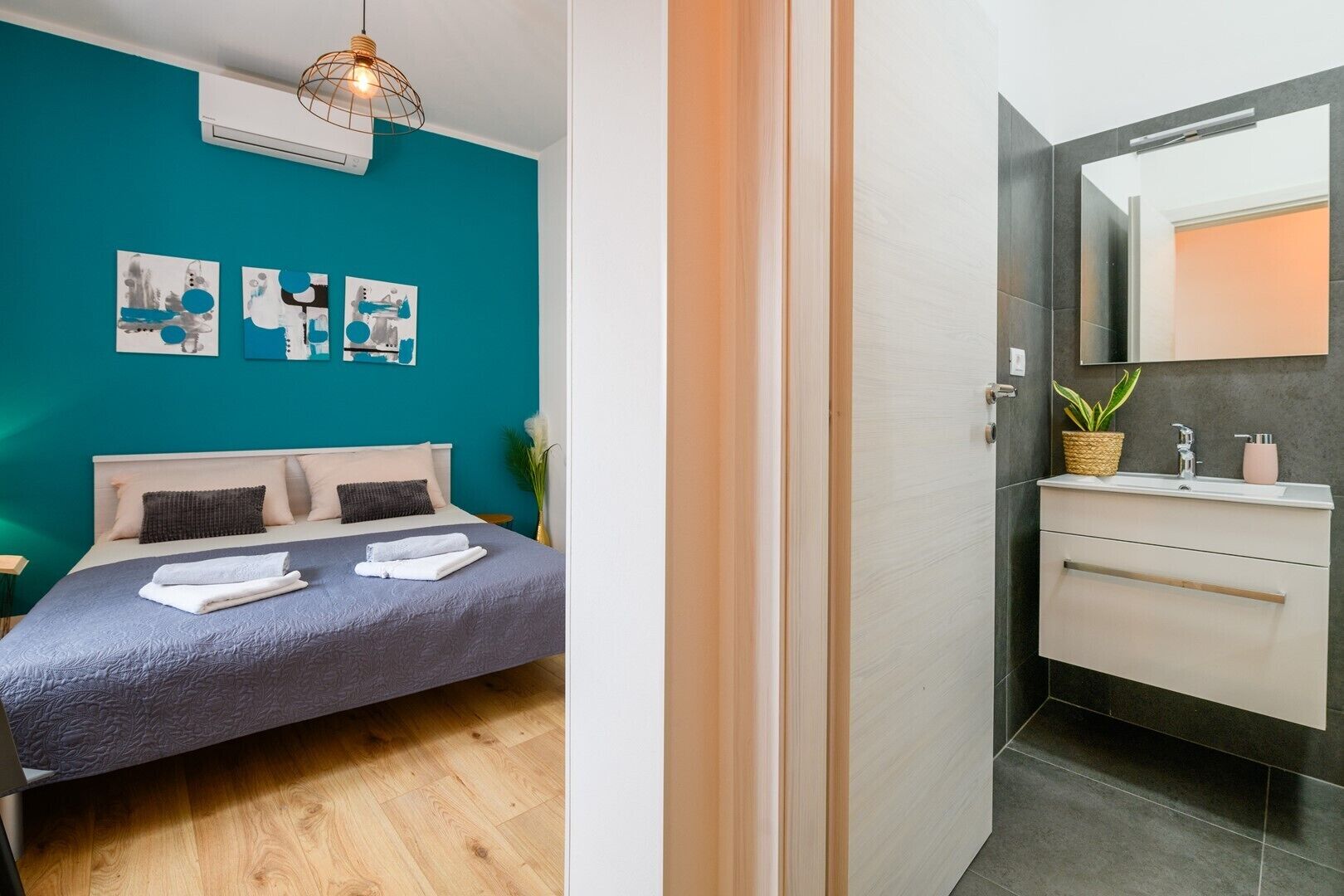 Une chambre moderne avec un mur de couleur turquoise, un lit recouvert d’une courtepointe grise et trois œuvres d’art abstraites accrochées au mur.
