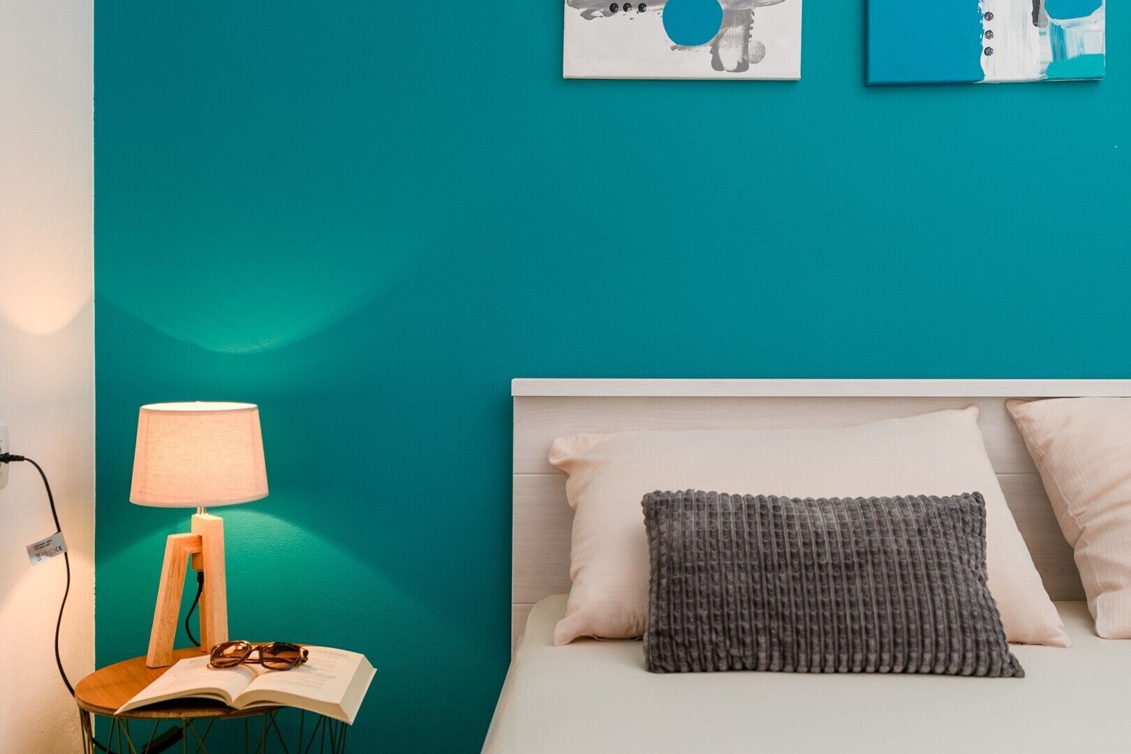 Een kamer in teal met een bed, een nachtkastje met een lamp en een boek.