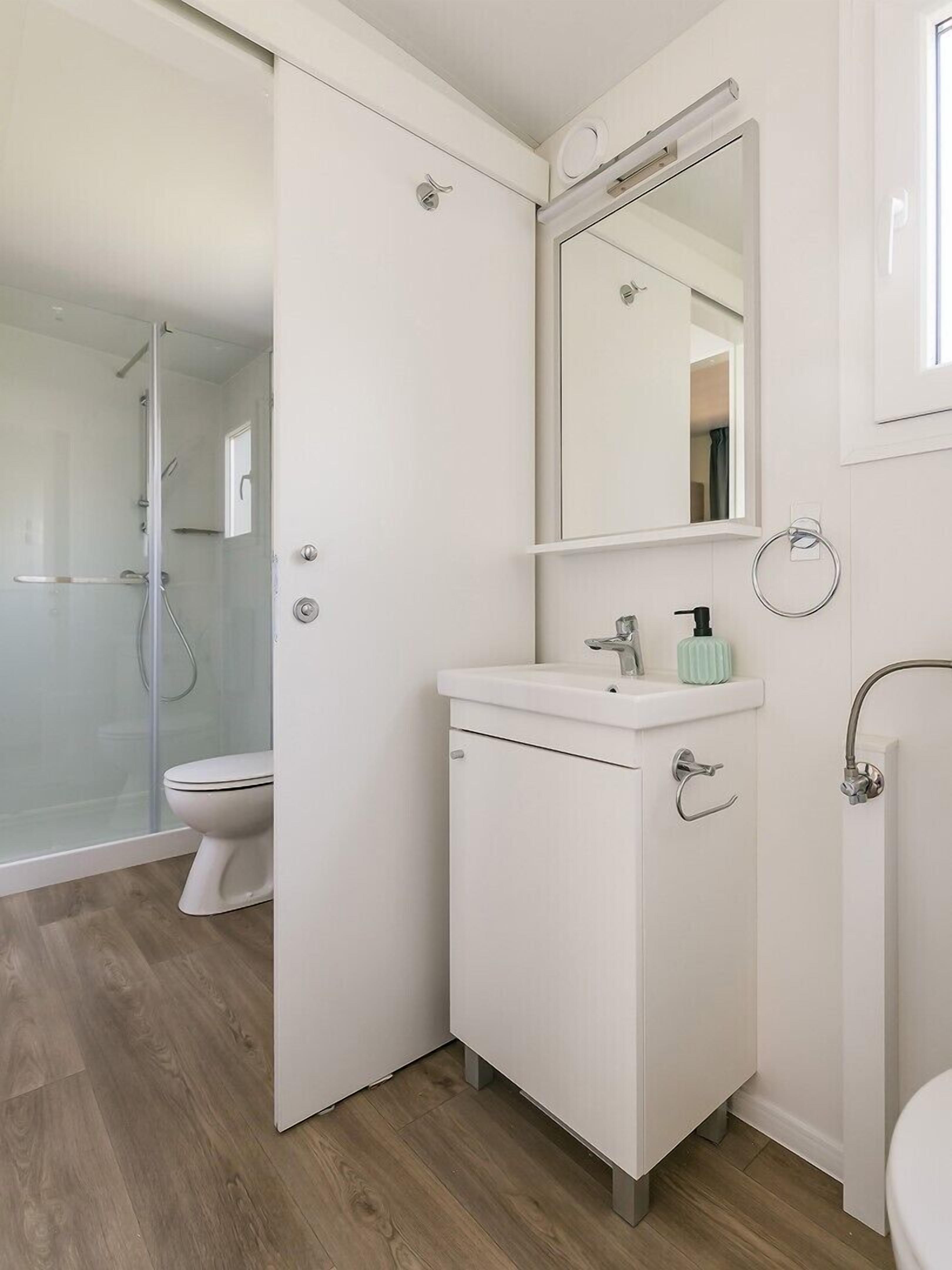 Een moderne badkamer met een douchecabine van glas, een witte wastafel met zeepdispenser en een spiegel boven de wastafel.
