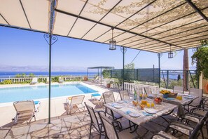 Un espace aménagé au bord de la piscine, avec une table dressée pour les repas, des chaises longues et une vue sur la mer.