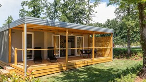 Una cabaña moderna de un piso con porche cubierto, puertas correderas de cristal y un pequeño espacio de estar al aire libre.