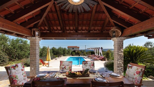An outdoor dining area with a pool and lounge chairs in the background.