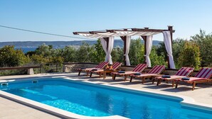 A swimming pool with lounge chairs and a pergola with white curtains.