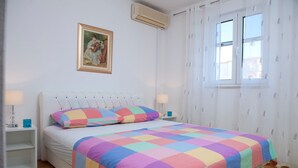 Ein Schlafzimmer mit einem Bett, einem Nachttisch, einem Fenster mit Vorhängen und einem Gemälde an der Wand.