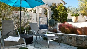 Ein Sitzbereich im Freien mit zwei Lounge-Sesseln, einem Tisch und einem blauen Sonnenschirm.
