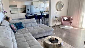 A modern living room with a grey sectional sofa, a round coffee table, and a pink armchair. A kitchen is visible in the background. - Villa Noura in Makarska, private pool,gym (Makarska)