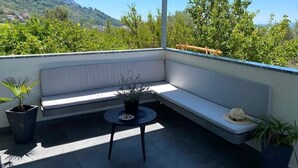 A balcony with a white cushioned bench, a small round table, and potted plants. - Villa Noura in Makarska, private pool,gym (Makarska)