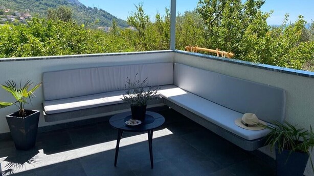 A balcony with a white cushioned bench, a small round table, and potted plants. - Villa Noura in Makarska, private pool,gym (Makarska)