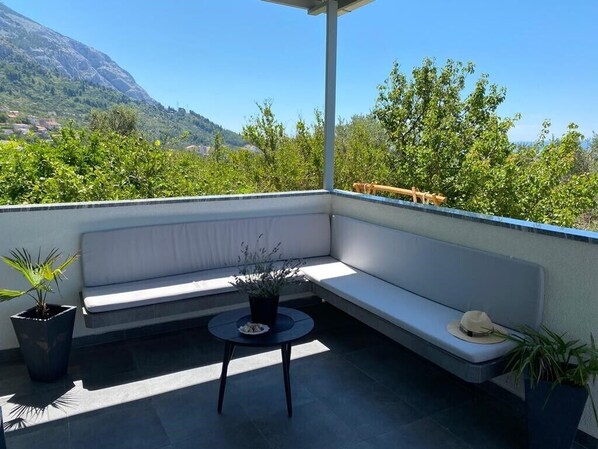 A balcony with a white cushioned bench, a small round table, and potted plants. - Villa Noura in Makarska, private pool,gym (Makarska)