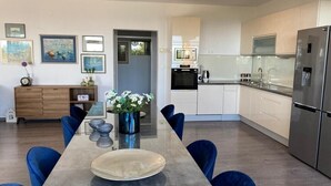 A modern kitchen with a dining area, featuring a long table, blue chairs, a refrigerator, and a microwave. - Villa Noura in Makarska, private pool,gym (Makarska)