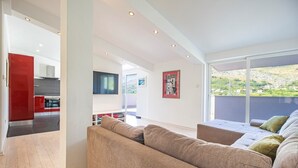 A modern living room with a large sofa, a television, and a view of the outdoors.