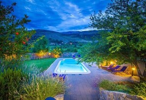 A swimming pool with lounge chairs and a stone pathway leading to it, surrounded by greenery and hills in the background. - Villa Leandra near Omiš, private pool (Tugare)