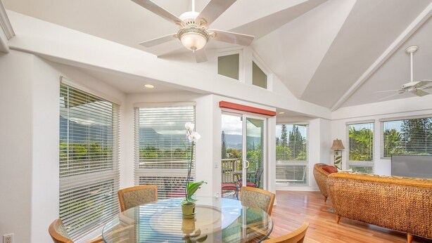 A spacious living area with a glass-top dining table, wicker sofa, and a ceiling fan. - Villas Of Kamalii 17 3 Bedroom Condo by RedAwning (Princeville)