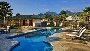 A swimming pool with lounge chairs, a building with a green roof, and mountains in the background. - Villas Of Kamalii 17 3 Bedroom Condo by RedAwning (Princeville)