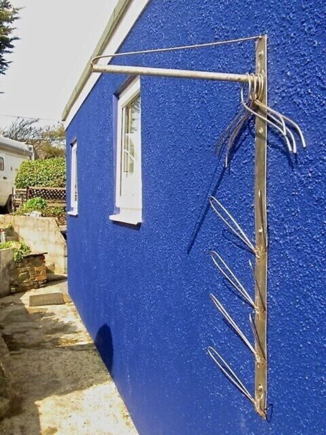 Un bâtiment bleu avec une structure métallique fixée au mur, une fenêtre et un chemin de pierre menant à un véhicule garé.