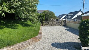 A stone pathway leading to a wooden gate, surrounded by greenery and residential buildings.