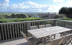 A wooden deck with a table and chairs, overlooking a rural landscape with fields and houses.