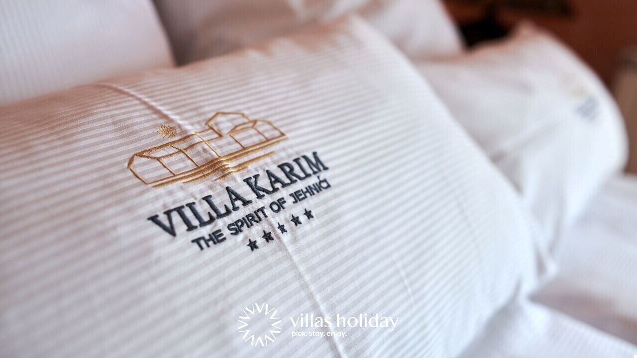 A pillow with embroidered text "VILLA KARIM THE SPIRIT OF JEHNIQ" and a logo.