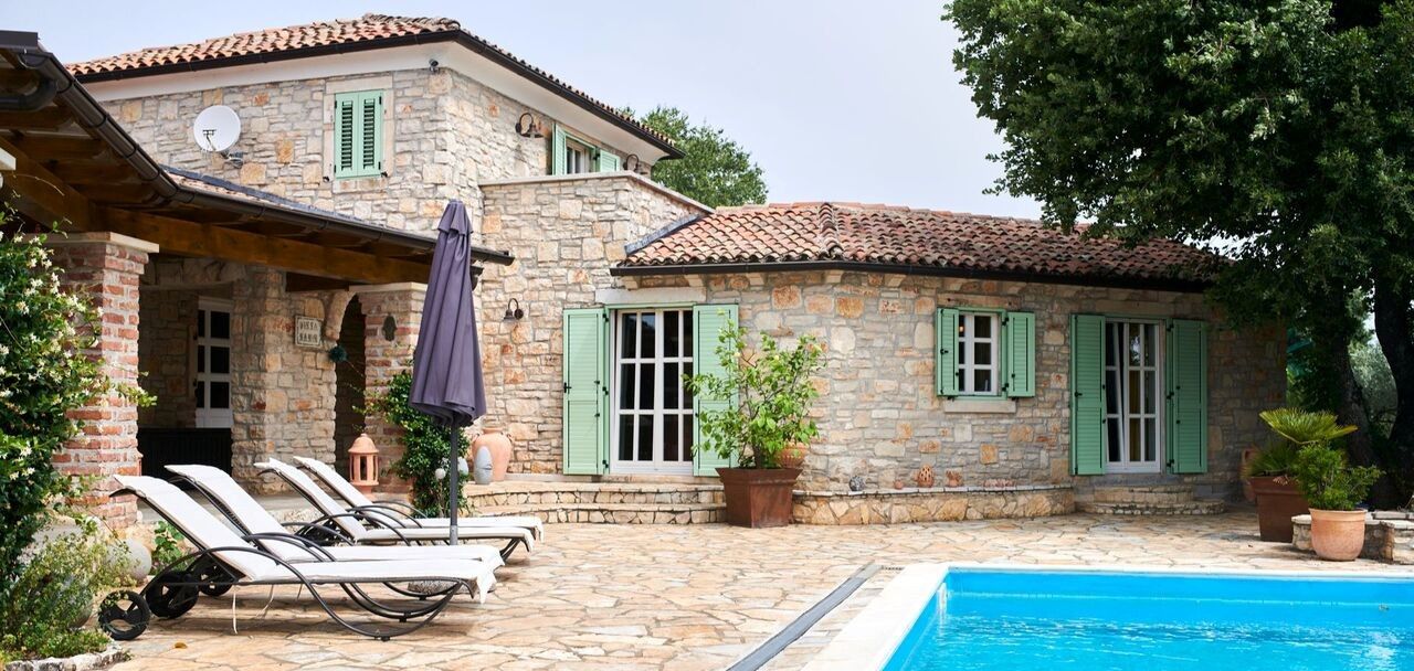 Una villa in pietra con piscina, area salotto esterna e giardino.