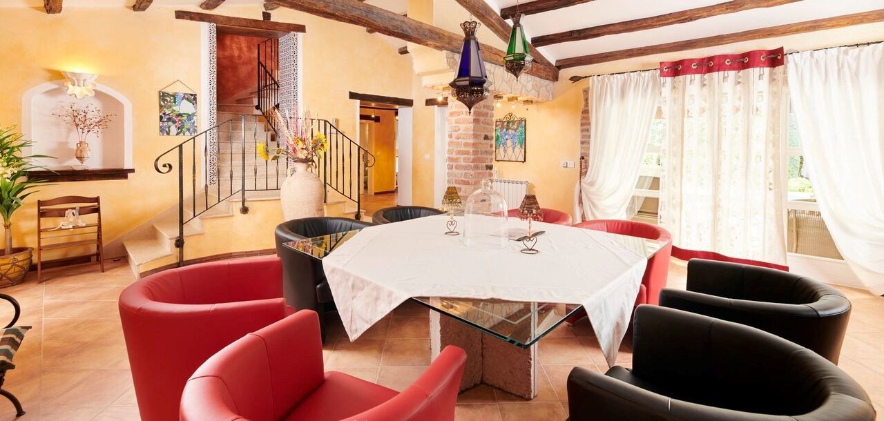 Un espace repas avec une table ronde, des chaises rouges et noires, et un escalier menant à un niveau supérieur.