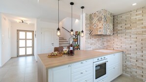 Une cuisine moderne dotée d’un grand îlot central, de meubles blancs, d’un four encastré et d’un dosseret décoré d’un motif en briques.
