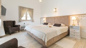 Une chambre à coucher avec un grand lit, des lampes de chevet, une chaise, une petite table et un téléviseur fixé au mur.